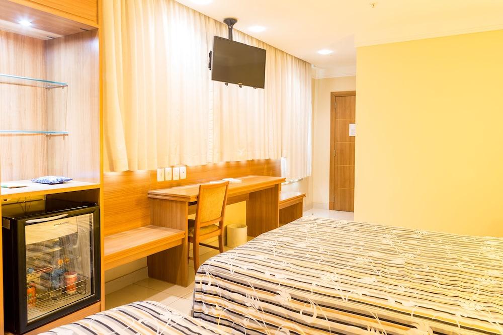 Hotel Atlantico Business Centro Ρίο ντε Τζανέιρο Εξωτερικό φωτογραφία The photo shows a hotel room with two beds featuring striped bedding. There is a wooden desk and chair near a window with light-colored curtains. A flat-screen television is mounted on the wall, and there appears to be a small refrigerator or mini-ba